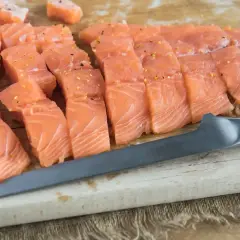 Pokrojony łosoś na desce, gotowy do przygotowania sushi. Widać kawałki ryby i nóż.