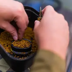 Ręce przygotowują zanętę, nabierając pellet z pojemnika. Dowiedz się, jak samemu zrobić pellet do wędkowania.