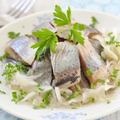 Pyszne śledzie w oleju z cebulką i natką pietruszki na talerzu.