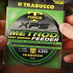 Ręce trzymają opakowanie żyłki Trabucco XPS Method Feeder. Idealna żyłka na grunt, która szybko tonie i jest odporna na przetarcia.