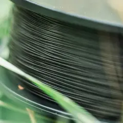 Nawinięta na szpulę ciemna żyłka na spinning, otoczona zieloną trawą. Idealna do łowienia drapieżników.