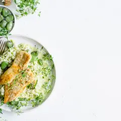 Aksamitne risotto z rybą, groszkiem i cukinią, ozdobione świeżym tymiankiem.