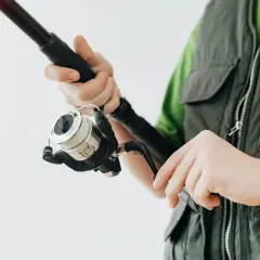Dłonie trzymające spinningową wędkę z kołowrotkiem. Czekam na branie.