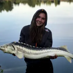 Uśmiechnięta wędkarz trzyma w rękach okazałego jesiotra. To wspaniały zestaw na jesiotra!
