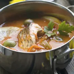 Aromatyczna zupa rybna z głową szczupaka, oliwkami i cytryną w metalowej misce.