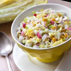 Lekka sałatka z surimi, jajka, kukurydzy i kapusty pekińskiej w żółtej miseczce. Obok łyżka.