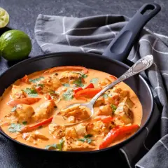 Aromatyczna zupa rybna z dorsza w kremowym sosie, z papryką i kolendrą, podana w czarnej patelni.