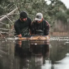 Dwóch wędkarzy trzyma w wodzie dużego karpia. Węzeł spinningowy, który pozwolił na ten połów, jest niewidoczny, ale zasługuje na uznanie.
