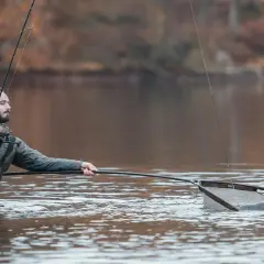 Wędkarz w wodzie z podbierakiem, gotowy do podebrania suma. Zestaw na suma z brzegu w akcji.