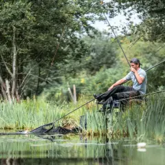 Wędkarz zmagający się z rybą, której wymiar lina jest kluczowy. W tle bujna zieleń i spokojna woda.