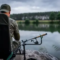 Wędkarz w kamuflażu czeka na branie. Jaka wędka na feeder sprawdzi się najlepiej w takich warunkach?