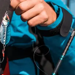 Dłoń trzyma błyszczącą przynętę, gotową do zarzucenia z kołowrotkiem do lekkiego spinningu.