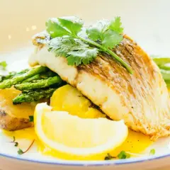 Szybki obiad z rybą: soczysty filet rybny z pieczonymi ziemniakami, szparagami i cytryną, udekorowany świeżą kolendrą.