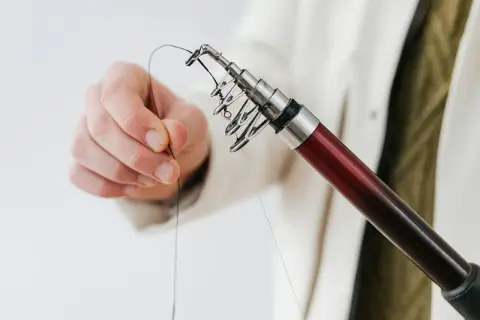 Dłoń przygotowuje się do wędkowania, pokazując, jak połączyć żyłkę z plecionką na końcu wędki.