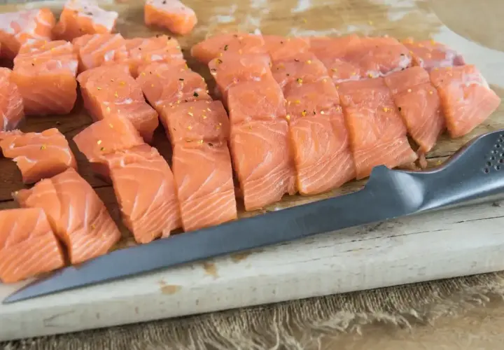 Pokrojony łosoś na desce, gotowy do przygotowania sushi. Widać kawałki ryby i nóż.