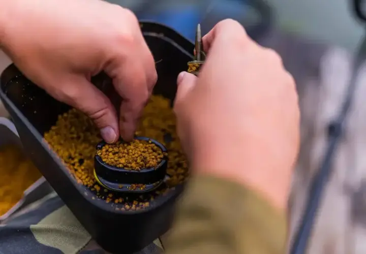 Ręce przygotowują zanętę, nabierając pellet z pojemnika. Dowiedz się, jak samemu zrobić pellet do wędkowania.