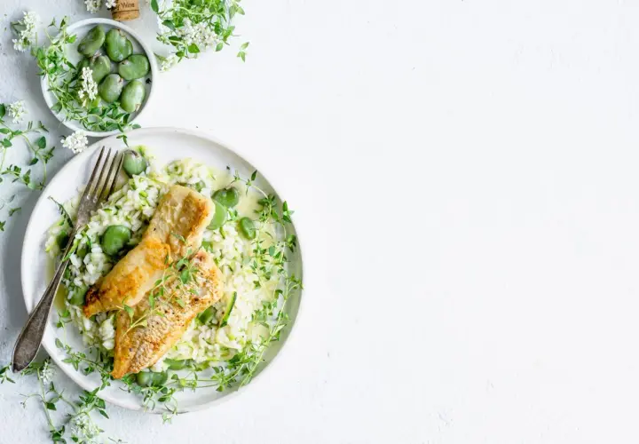 Aksamitne risotto z rybą, groszkiem i cukinią, ozdobione świeżym tymiankiem.