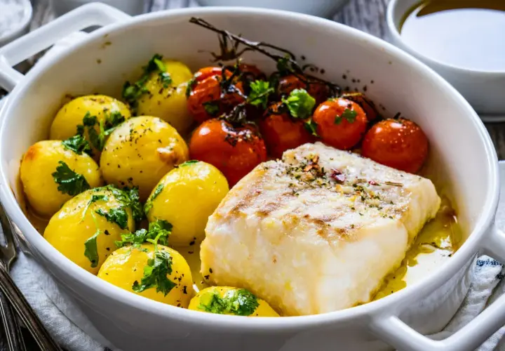 Pyszne dania z ryby: pieczony filet z dorsza z ziemniaczkami i pomidorkami koktajlowymi, posypane ziołami.