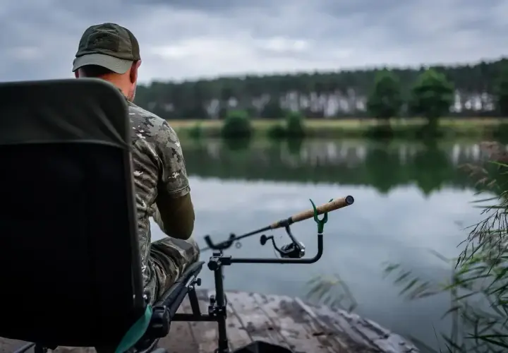 Wędkarz w kamuflażu czeka na branie. Jaka wędka na feeder sprawdzi się najlepiej w takich warunkach?