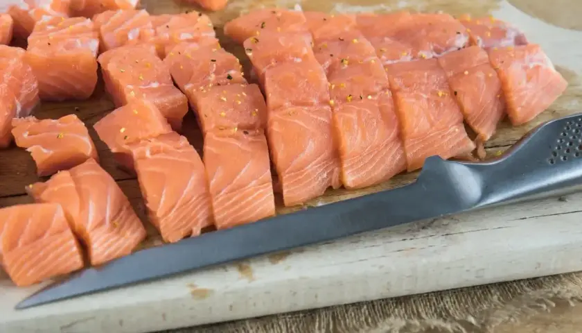 Pokrojony łosoś na desce, gotowy do przygotowania sushi. Widać kawałki ryby i nóż.