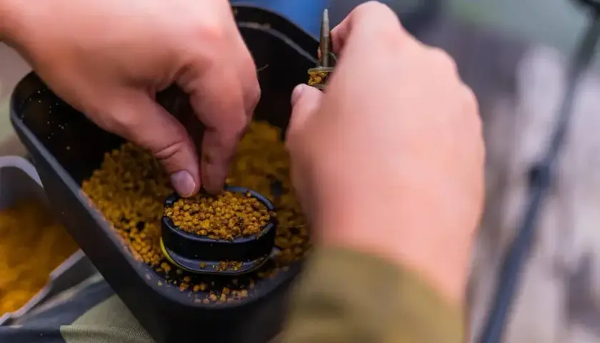 Ręce przygotowują zanętę, nabierając pellet z pojemnika. Dowiedz się, jak samemu zrobić pellet do wędkowania.