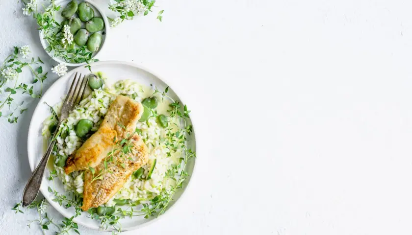 Aksamitne risotto z rybą, groszkiem i cukinią, ozdobione świeżym tymiankiem.