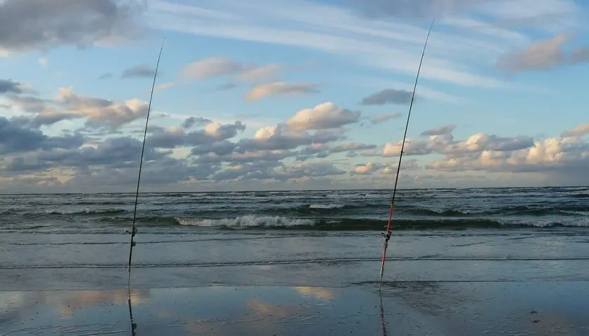 Dwa wędki stoją na plaży, gotowe do trollingu wędkarstwa. Morze faluje pod chmurami.