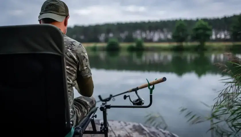Wędkarz w kamuflażu czeka na branie. Jaka wędka na feeder sprawdzi się najlepiej w takich warunkach?