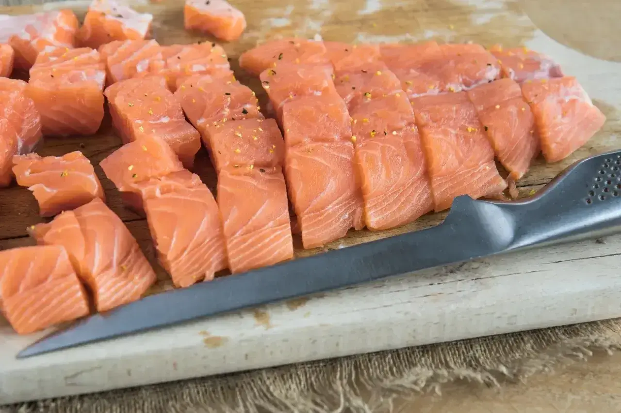 Pokrojony łosoś na desce, gotowy do przygotowania sushi. Widać kawałki ryby i nóż.