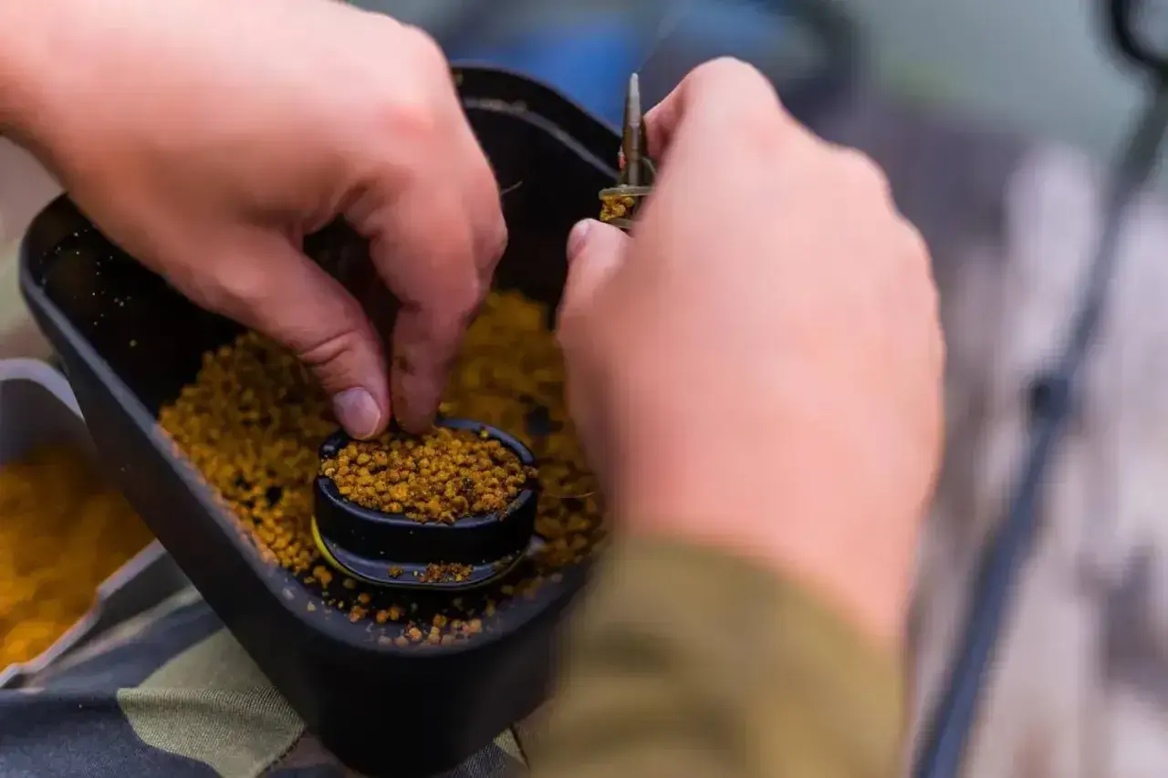 Ręce przygotowują zanętę, nabierając pellet z pojemnika. Dowiedz się, jak samemu zrobić pellet do wędkowania.