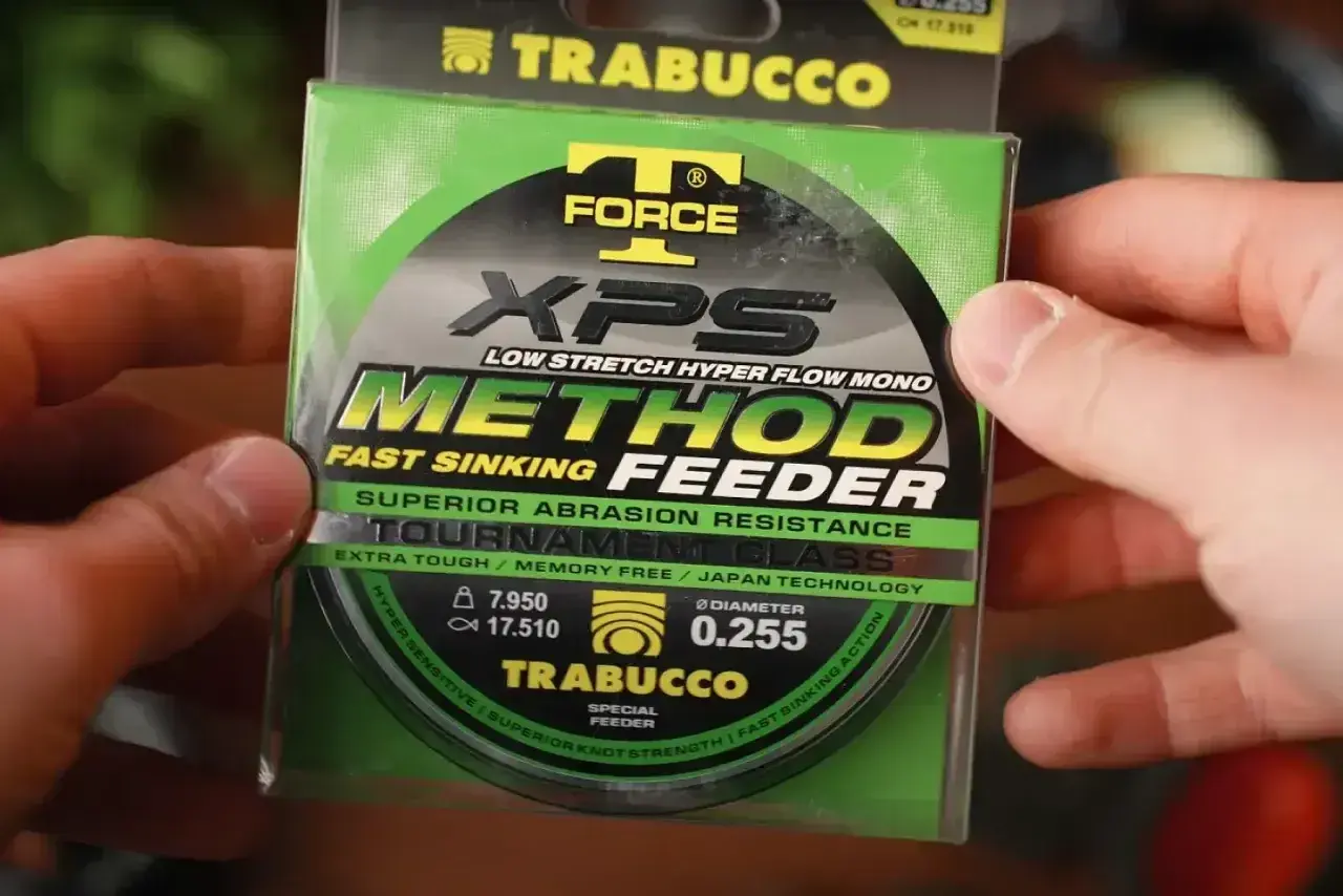 Ręce trzymają opakowanie żyłki Trabucco XPS Method Feeder. Idealna żyłka na grunt, która szybko tonie i jest odporna na przetarcia.