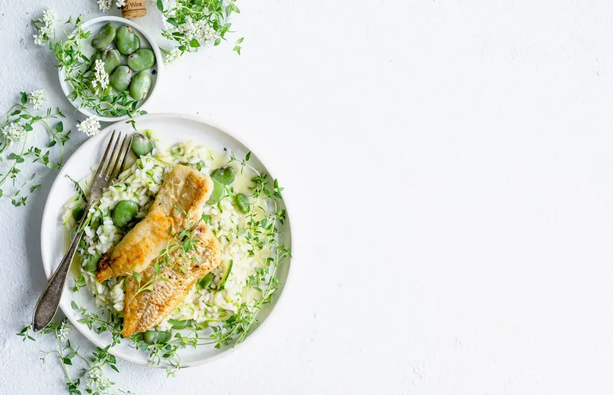 Aksamitne risotto z rybą, groszkiem i cukinią, ozdobione świeżym tymiankiem.