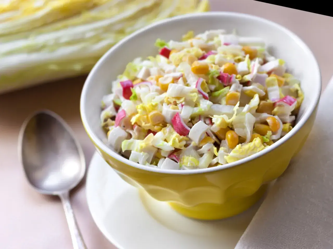 Lekka sałatka z surimi, jajka, kukurydzy i kapusty pekińskiej w żółtej miseczce. Obok łyżka.