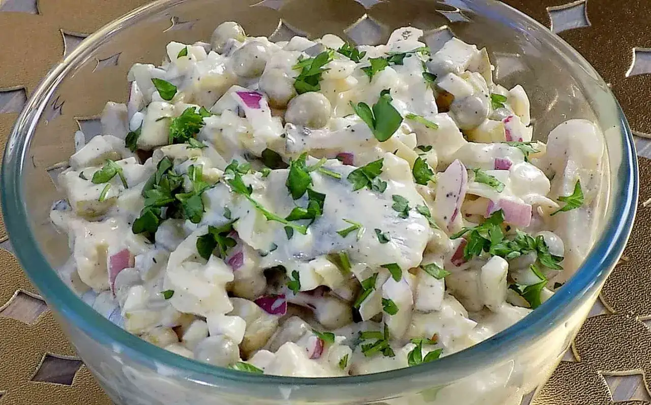 Pyszna sałatka ze śledzi solonych z ziemniakami, jajkiem, cebulą i groszkiem, polana kremowym sosem i posypana natką pietruszki.