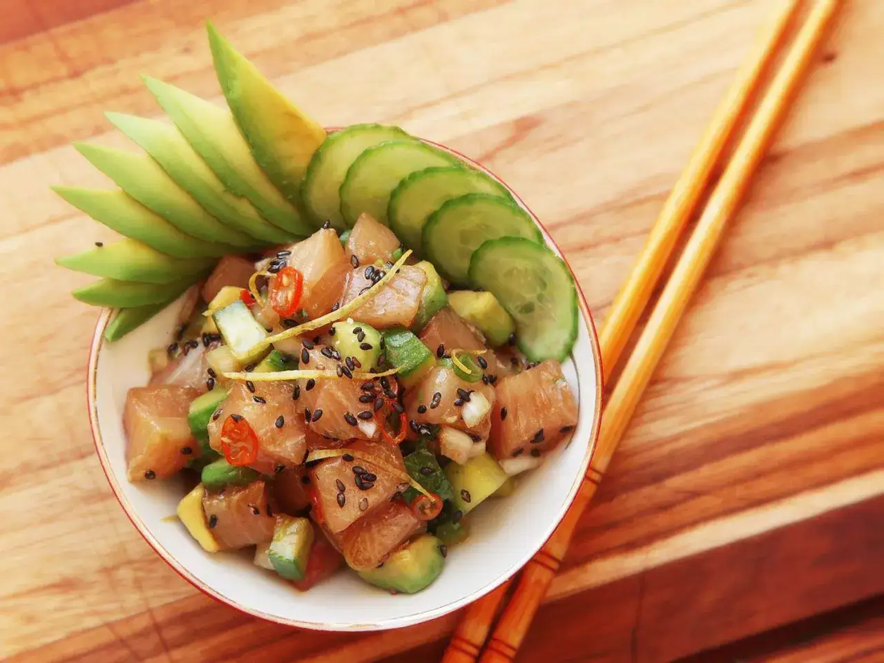 Pyszne dania z ryb na zimno: poke bowl z awokado, ogórkiem i sezamem, obok pałeczki.
