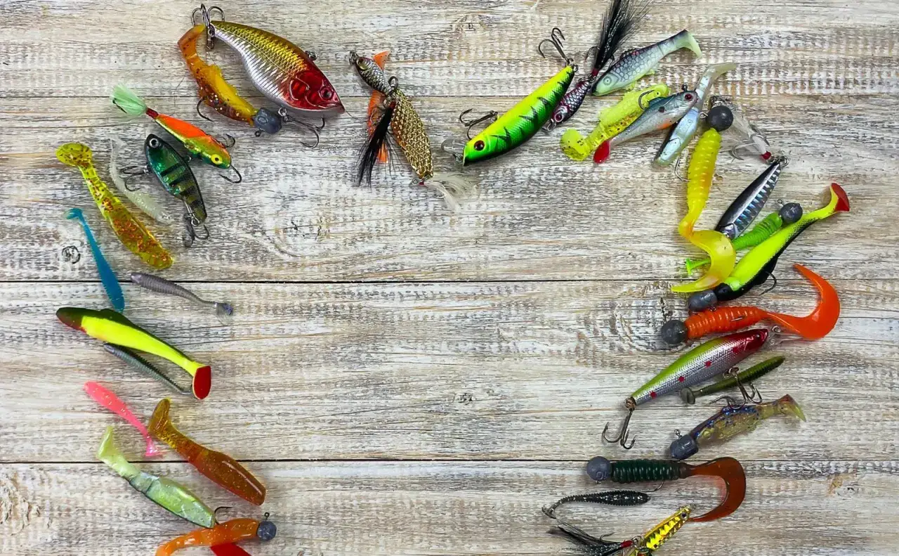Kolekcja kolorowych gum do spinningu, imitujących ryby i robaki, ułożona na drewnianym tle.
