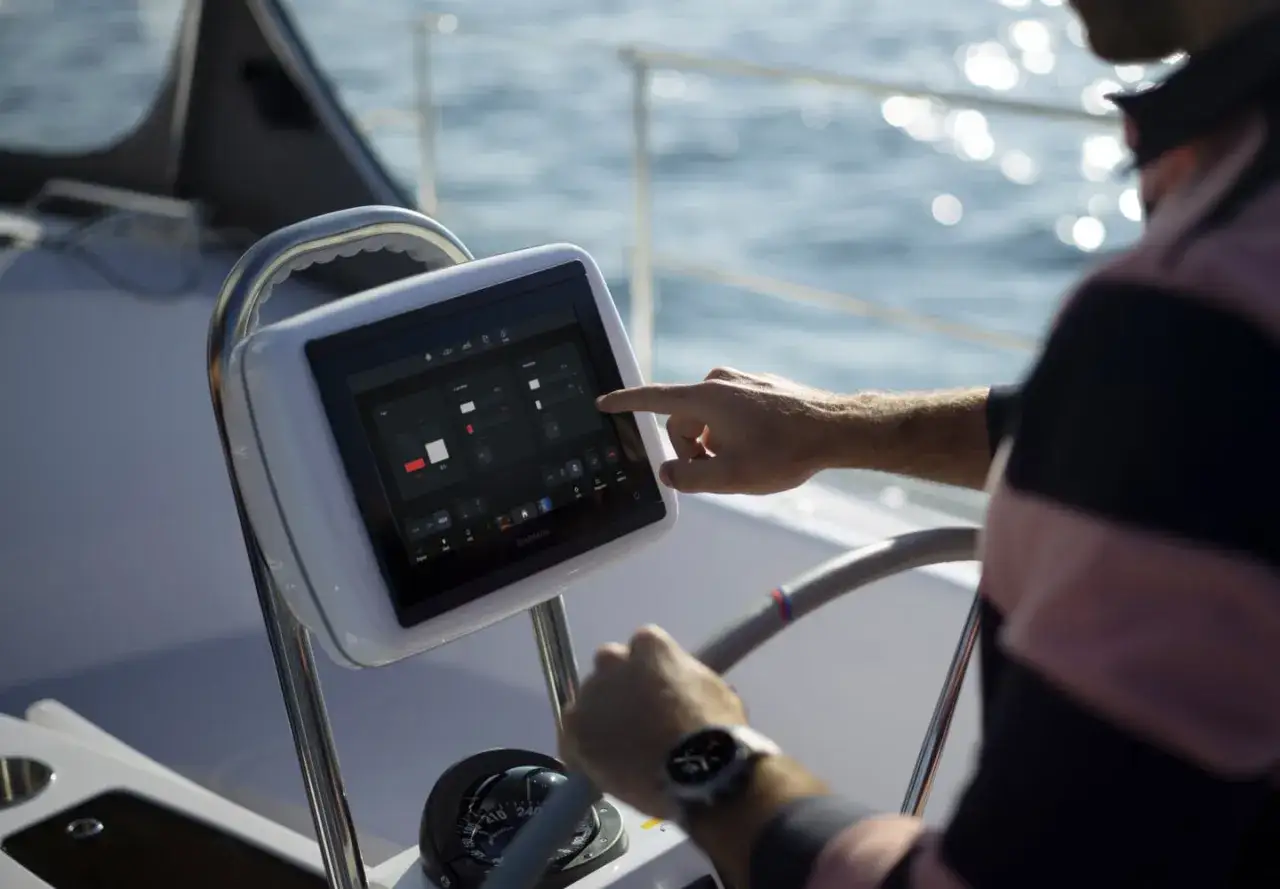Ręka dotyka ekranu nawigacyjnego Garmin na łodzi. Garmin to firma znana z urządzeń GPS i elektroniki.